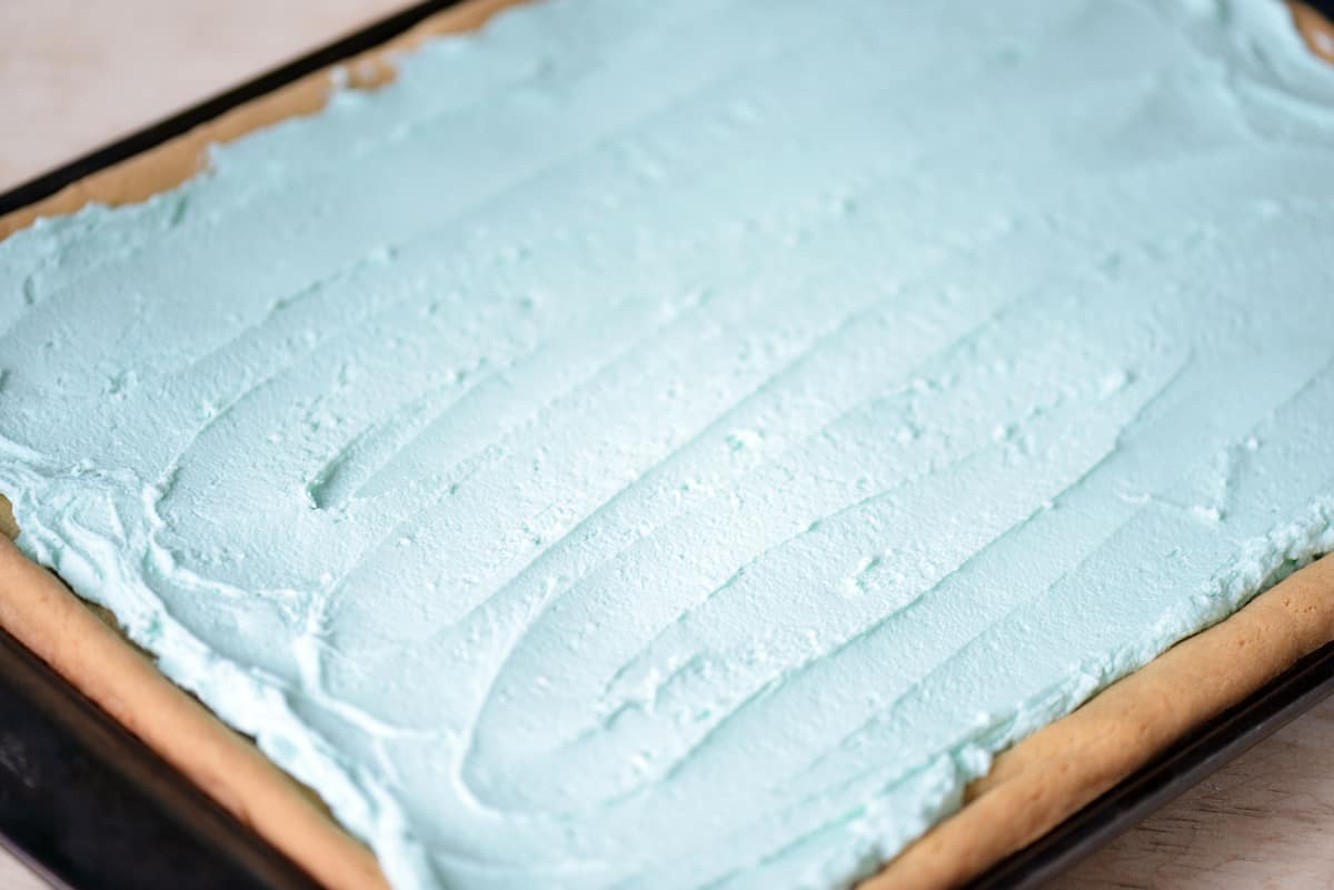 Blue buttercream frosting on cooled sugar cookie bars.