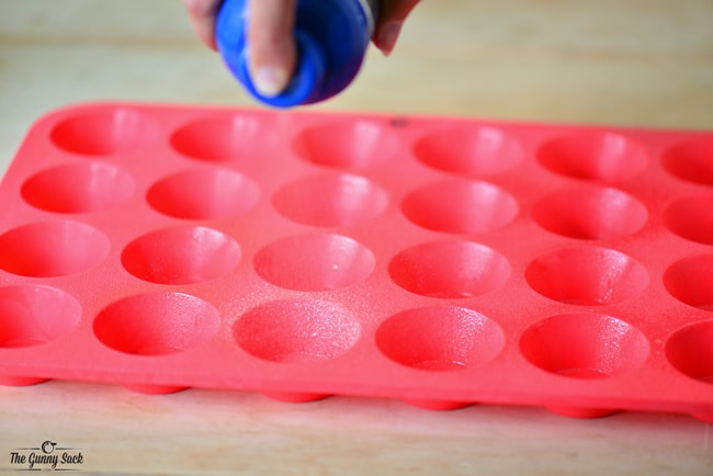 Spraying A Red Silicone Mini Muffin Pan With Cooking Spray