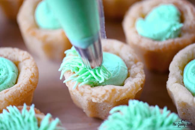 piping grass buttercream frosting into the Easter basket cookie cup