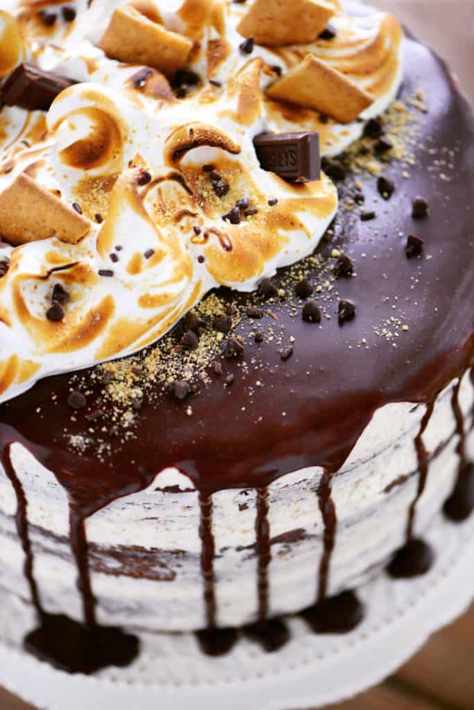 a smores cake topped with toasted meringue and chocolate ganache dribbles down the sides
