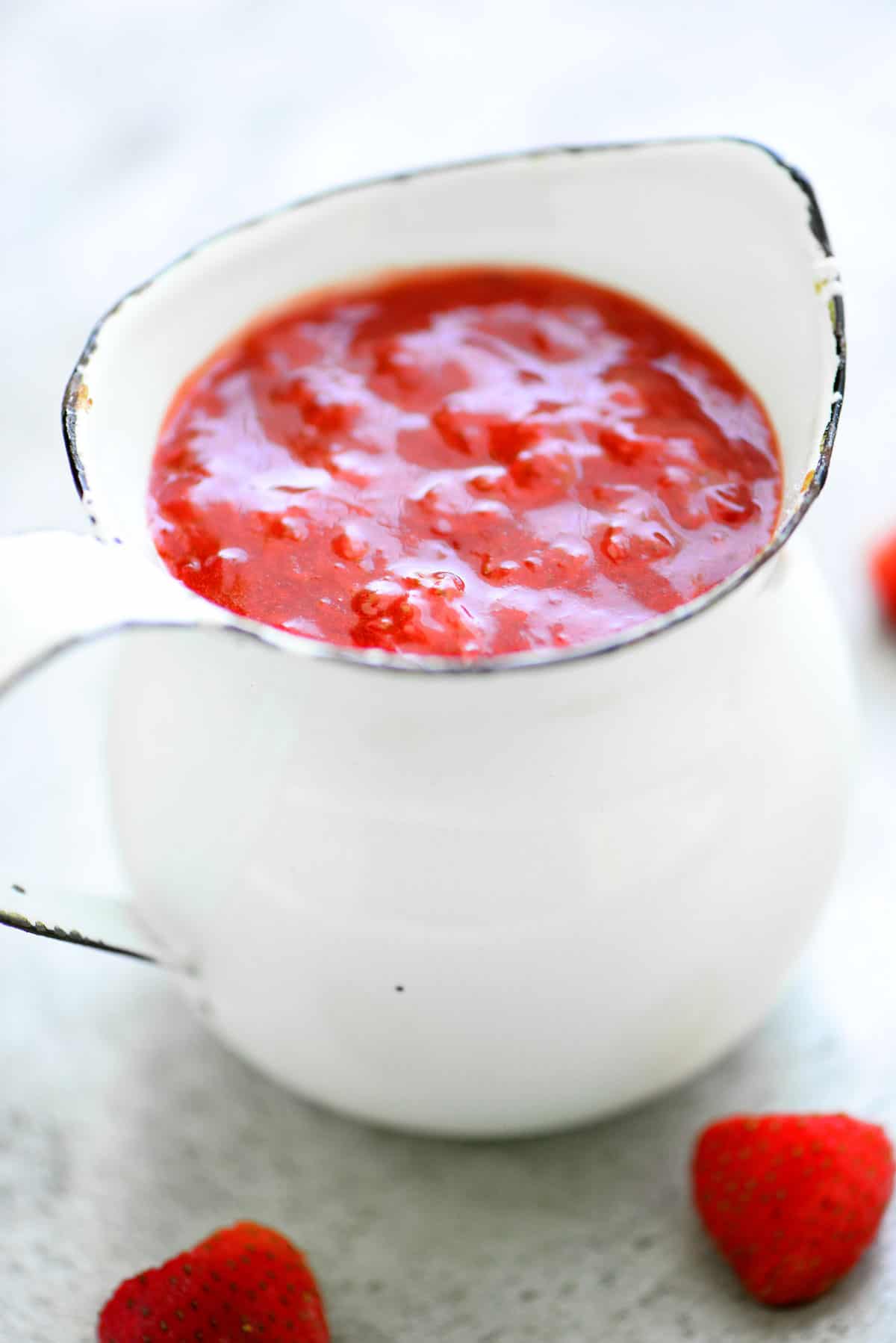 red sauce in a white pitcher with strawberries next to it