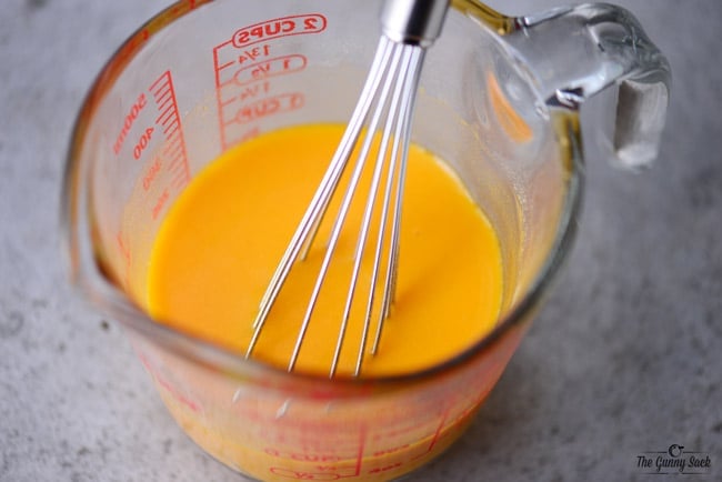 oil and powdered cheddar cheese being whisked in a glass measuring cup
