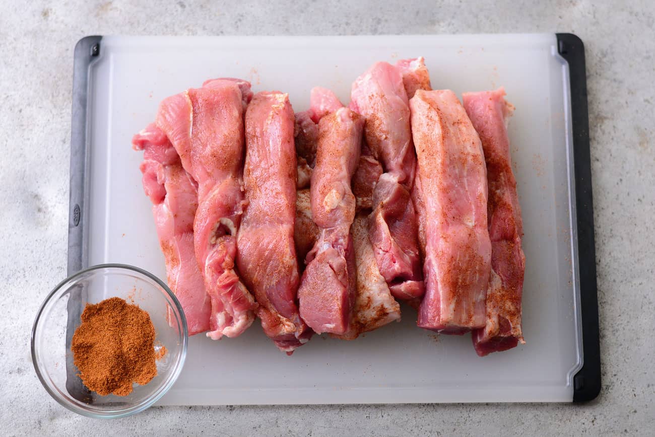 raw rib meat on a cutting board sprinkled with seasoning