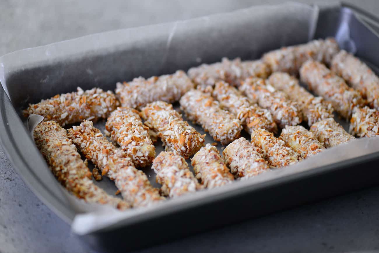coated cheese sticks on a pan with parchment paper