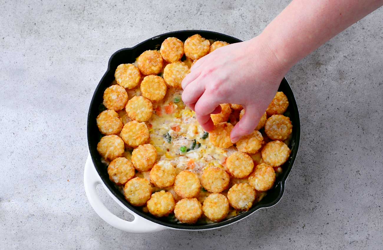 placing tater tots over other ingredients in the skillet