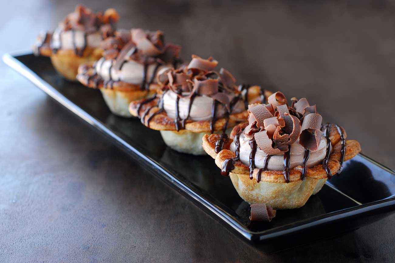 Four mini Nutella pies lined up on a black tray.