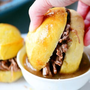 Slow cooker french dip sandwich being dipped into au jus in a white bowl.