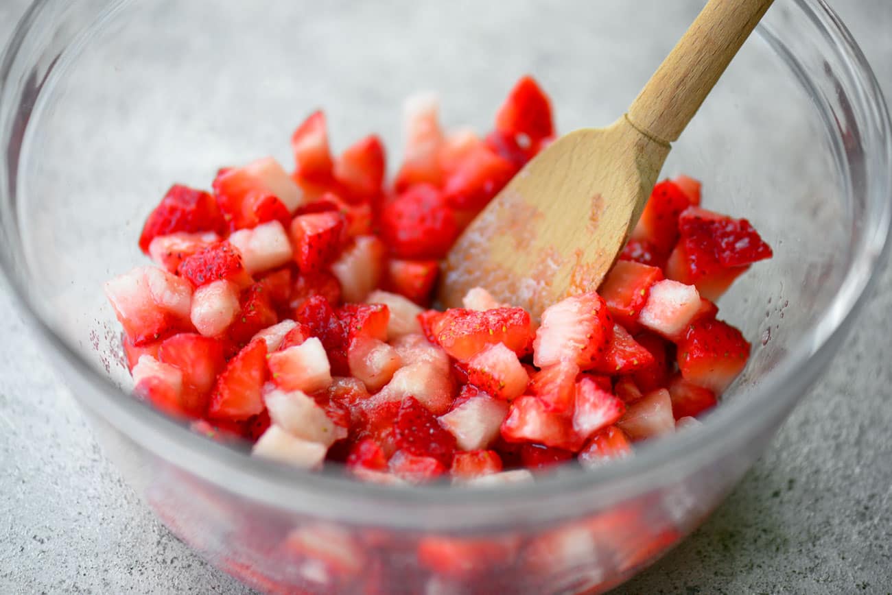 Chopped Strawberries Sprinkled With Sugar in a Bowl Being Mixed With a Wooden Spoon
