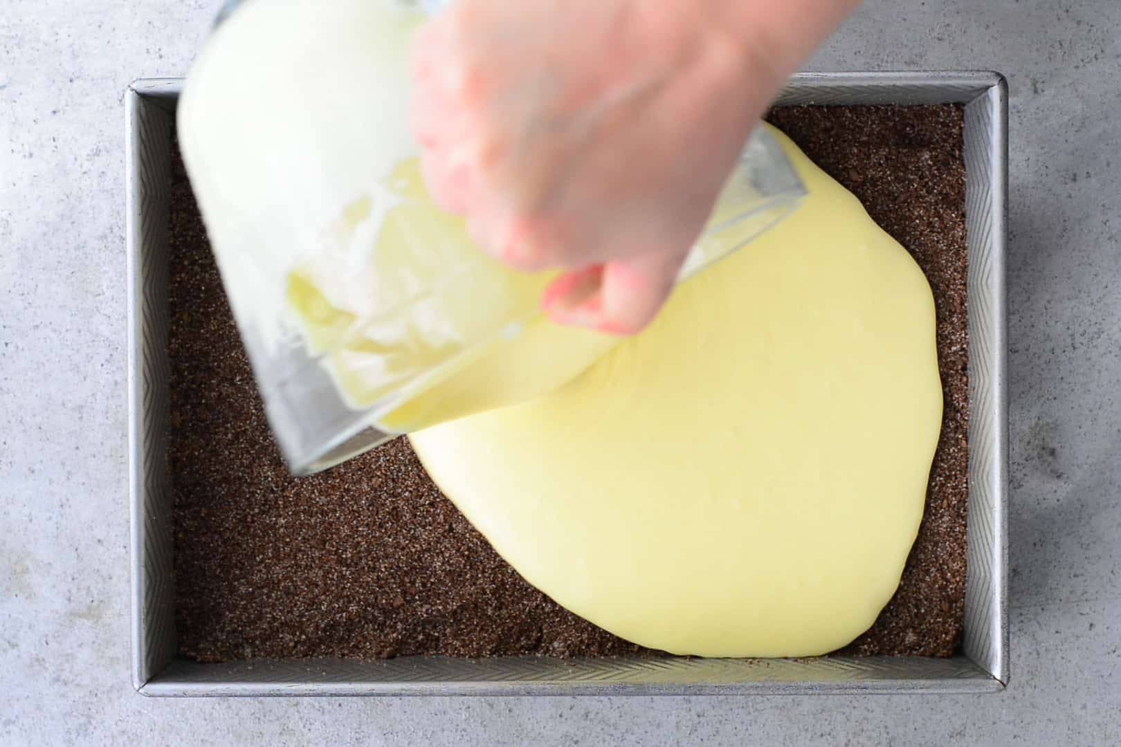 pouring cheesecake mixture over crust