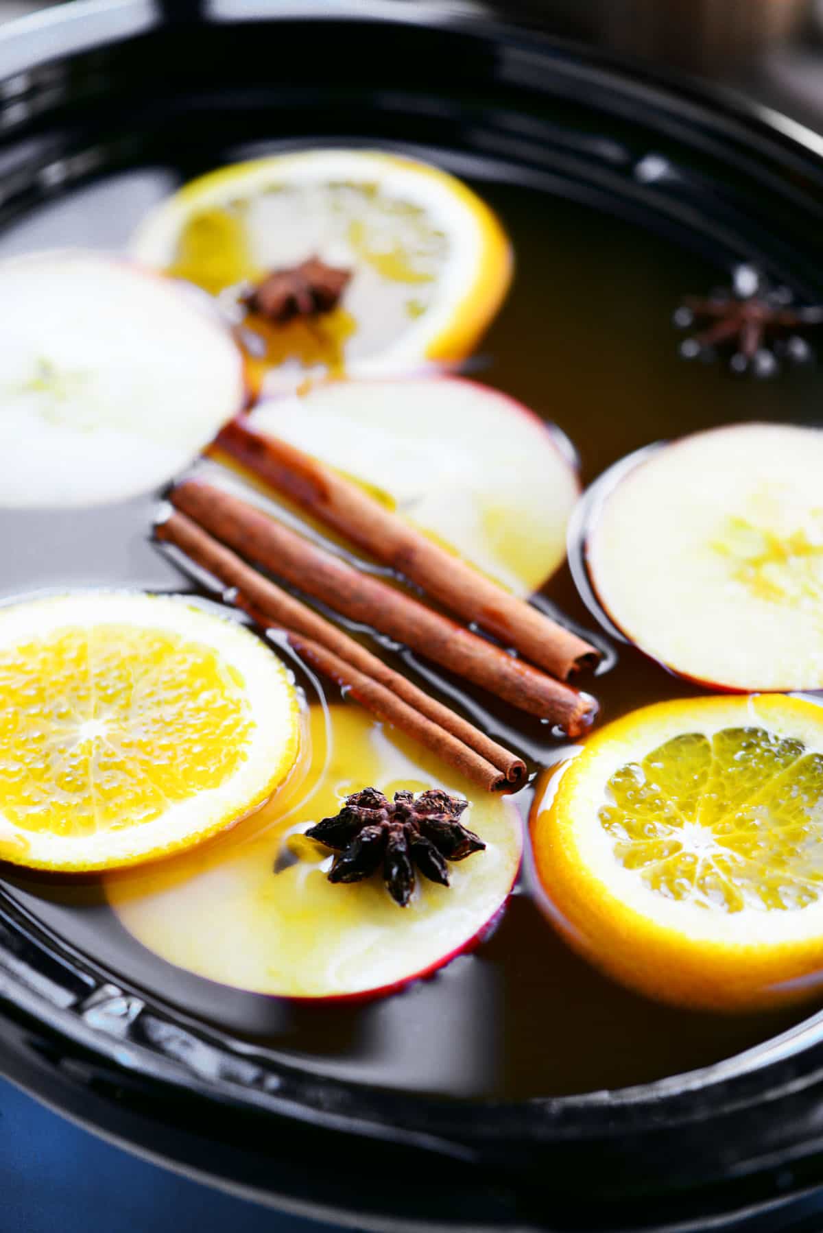 apple cider in a slow cooker with apple and orange slices cinnamon sticks and star anise