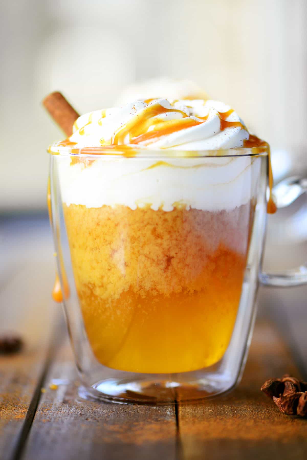  apple cider in a clear glass mug topped with caramel and whipped cream