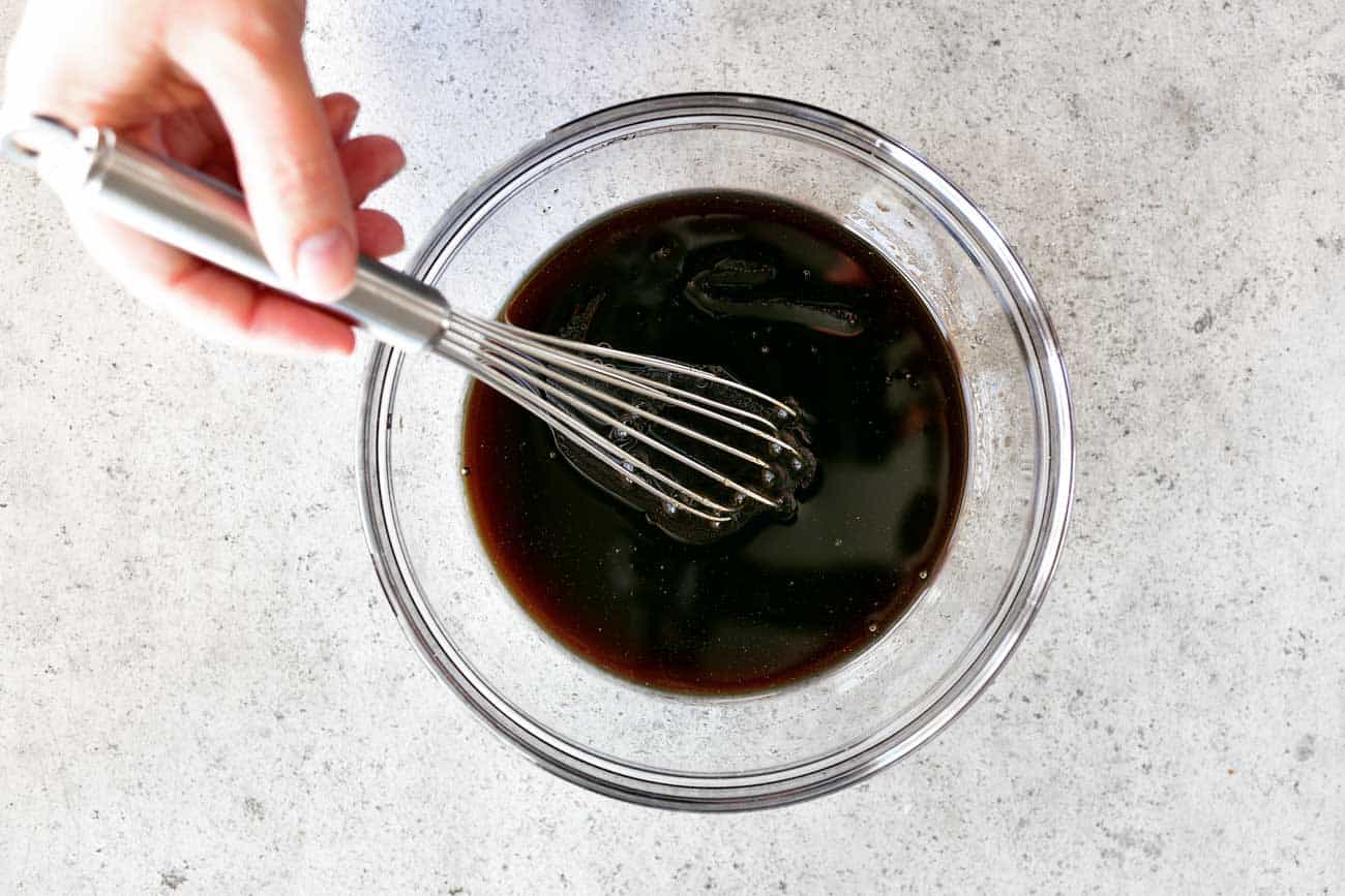 Dark sauce being whisked in a glass bowl.