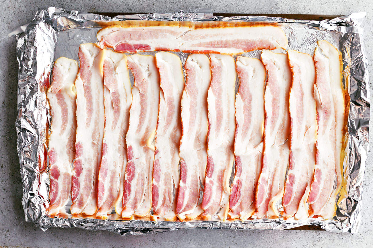 uncooked bacon lined up in a foil covered baking pan