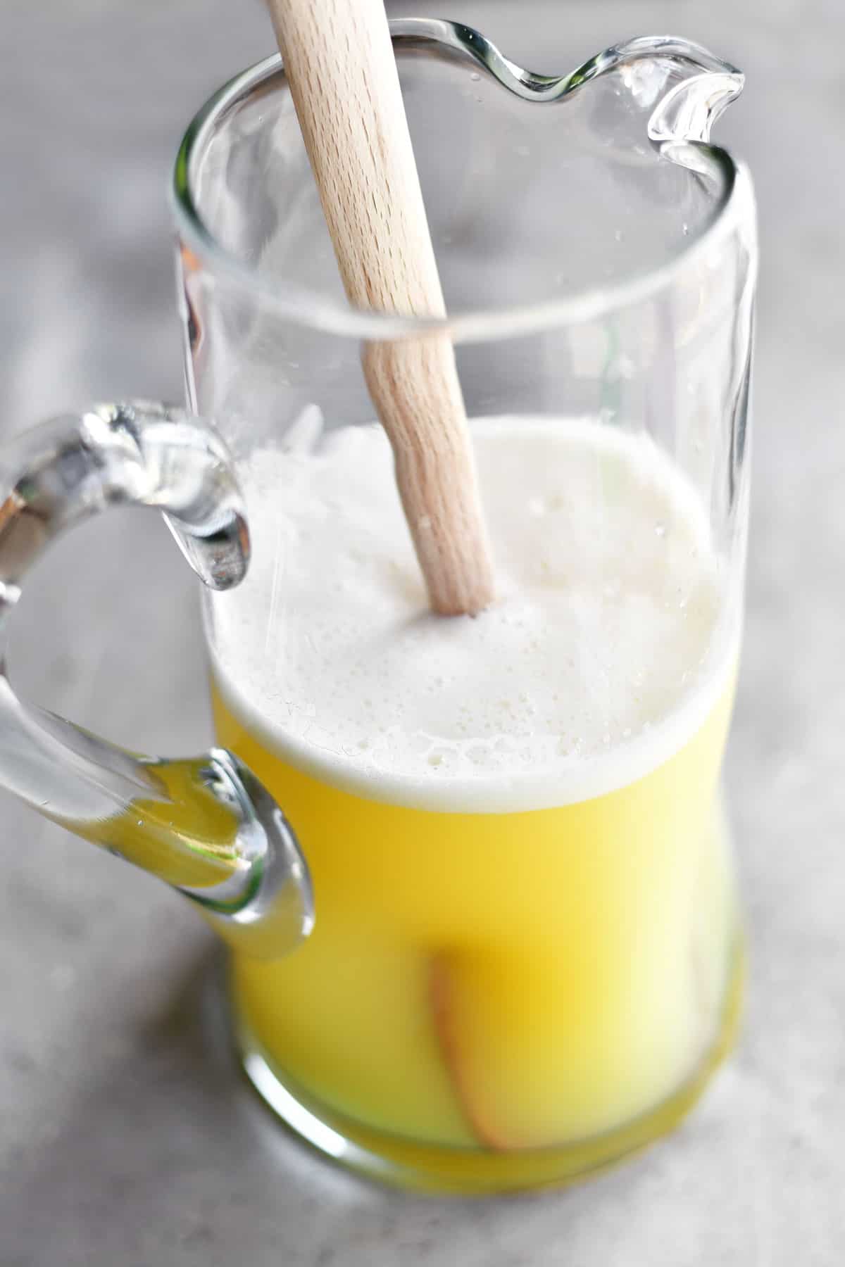 mixing lemon sherbet punch in a pitcher with a wooden spoon