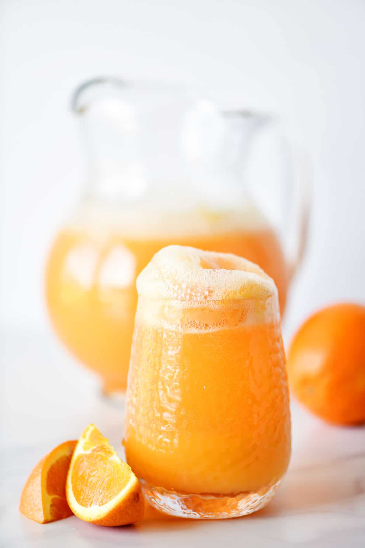 orange sherbet punch in a glass and pitcher with orange slices