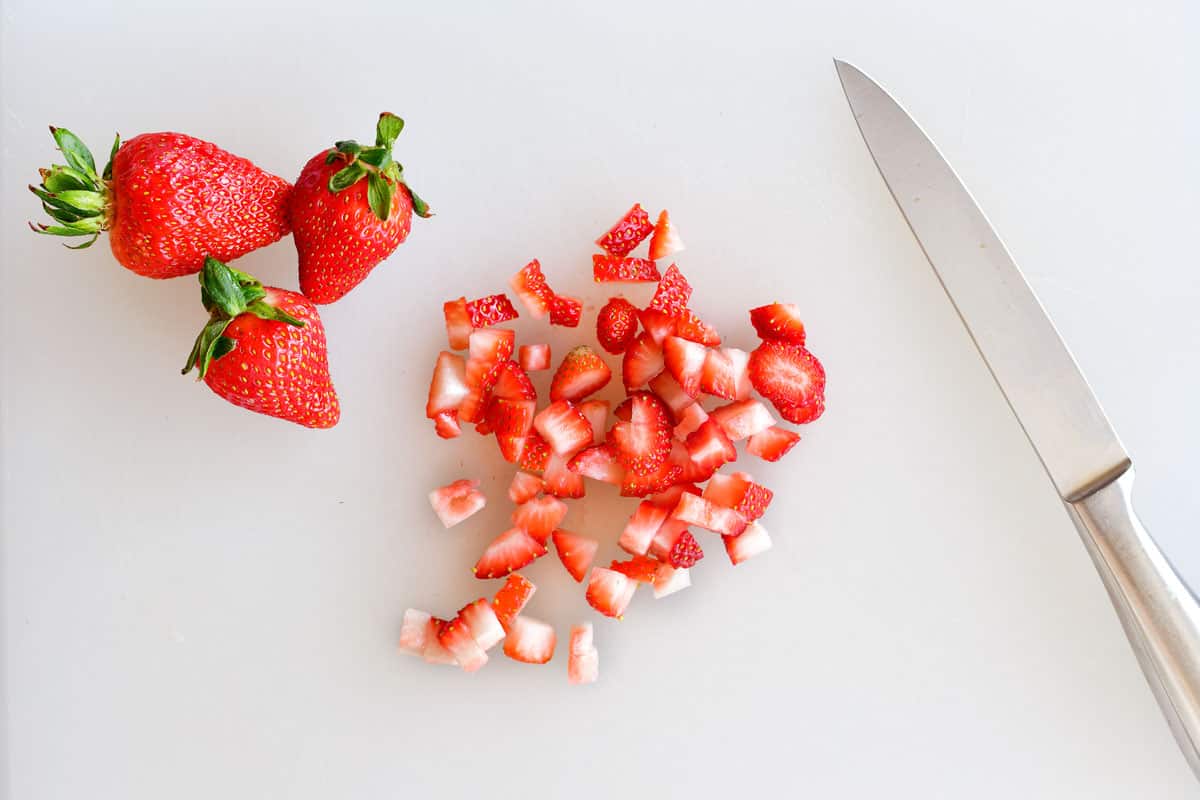 diced strawberries on a cutting board with a knife