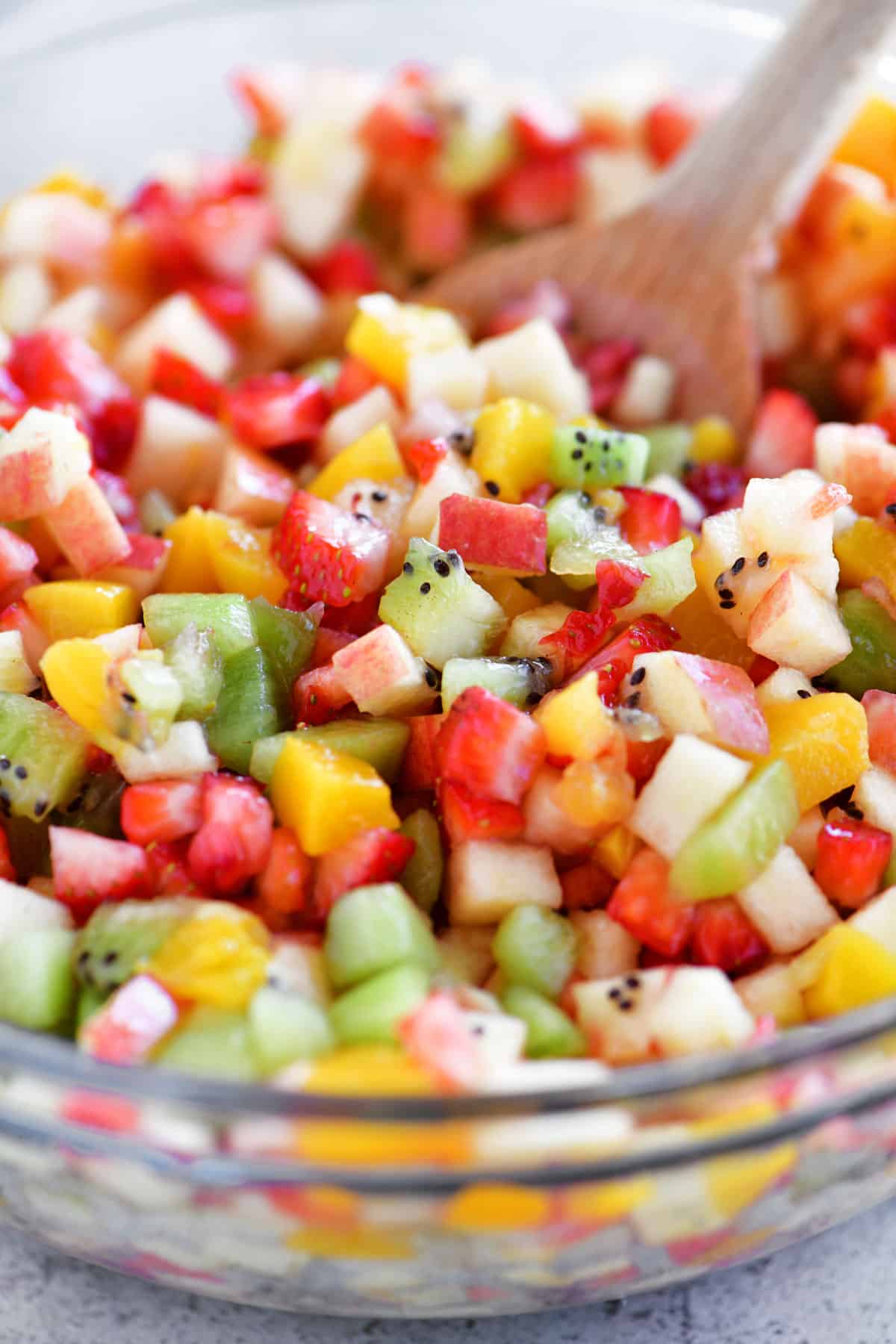fruit salsa in a glass bowl with a wooden spoon