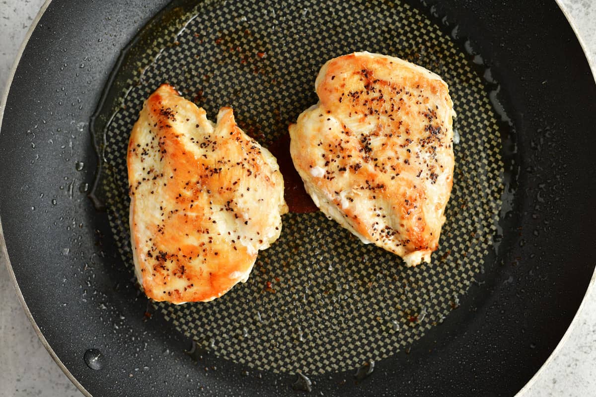 two cooked chicken breasts in a pan