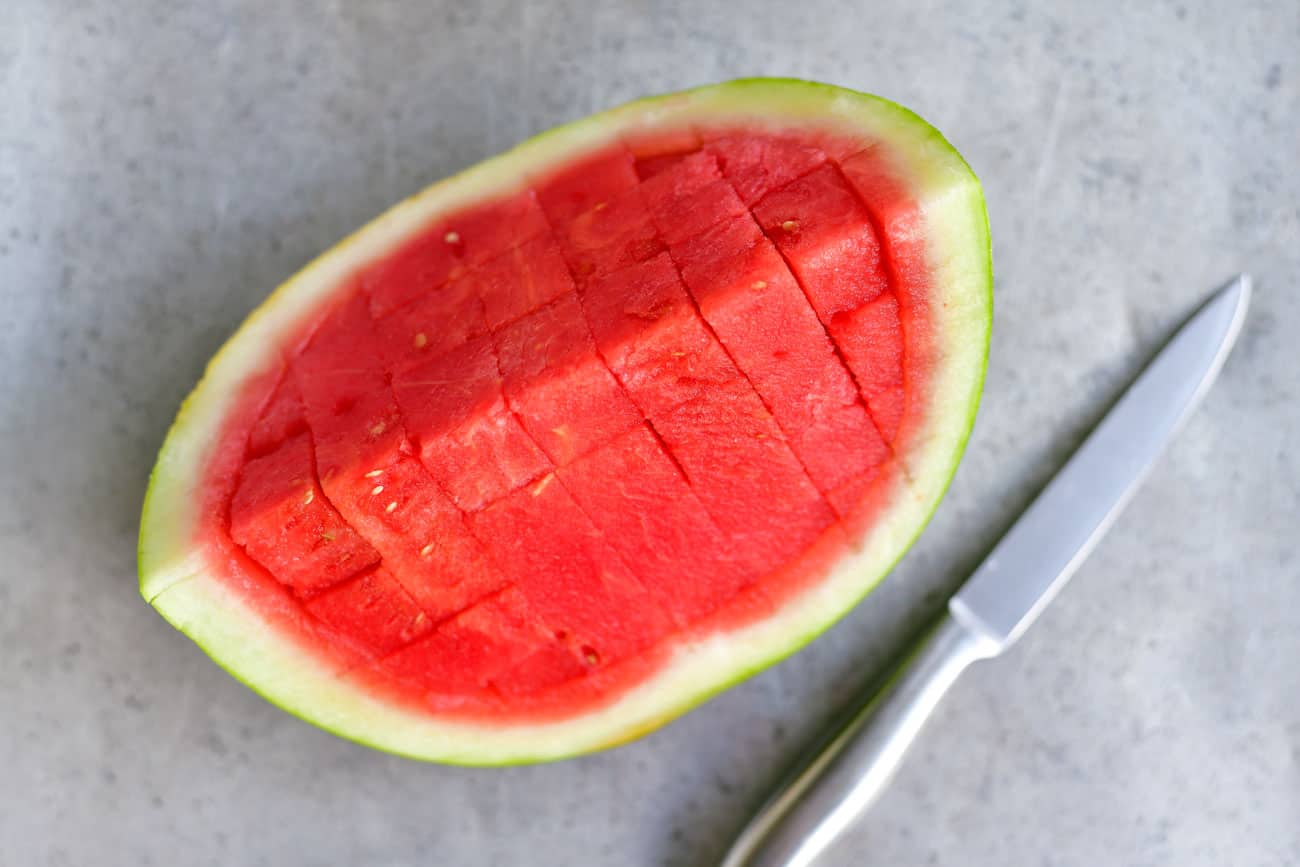 a quarter of a watermelon sliced into cubes with a pairing knife