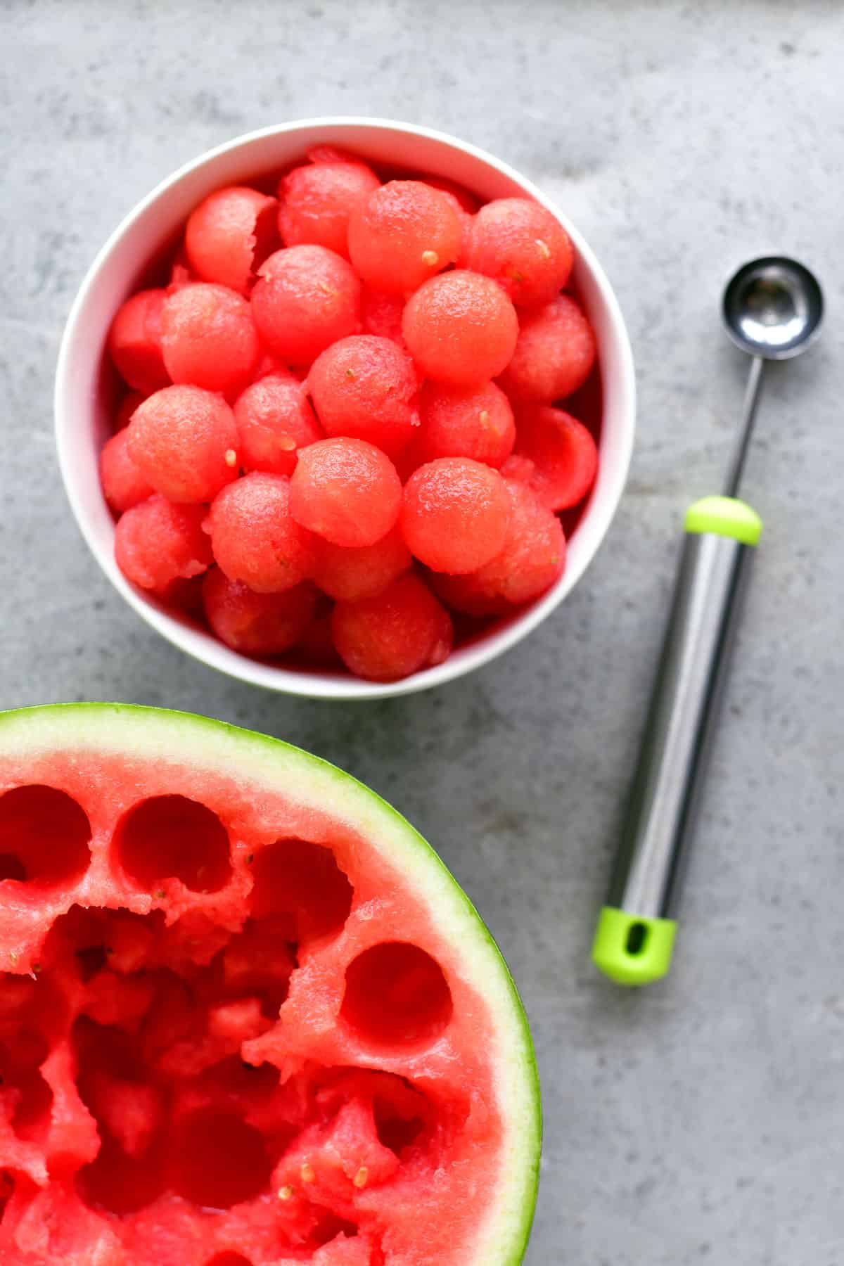 watermelon balls in a white bowl next to a melon baller