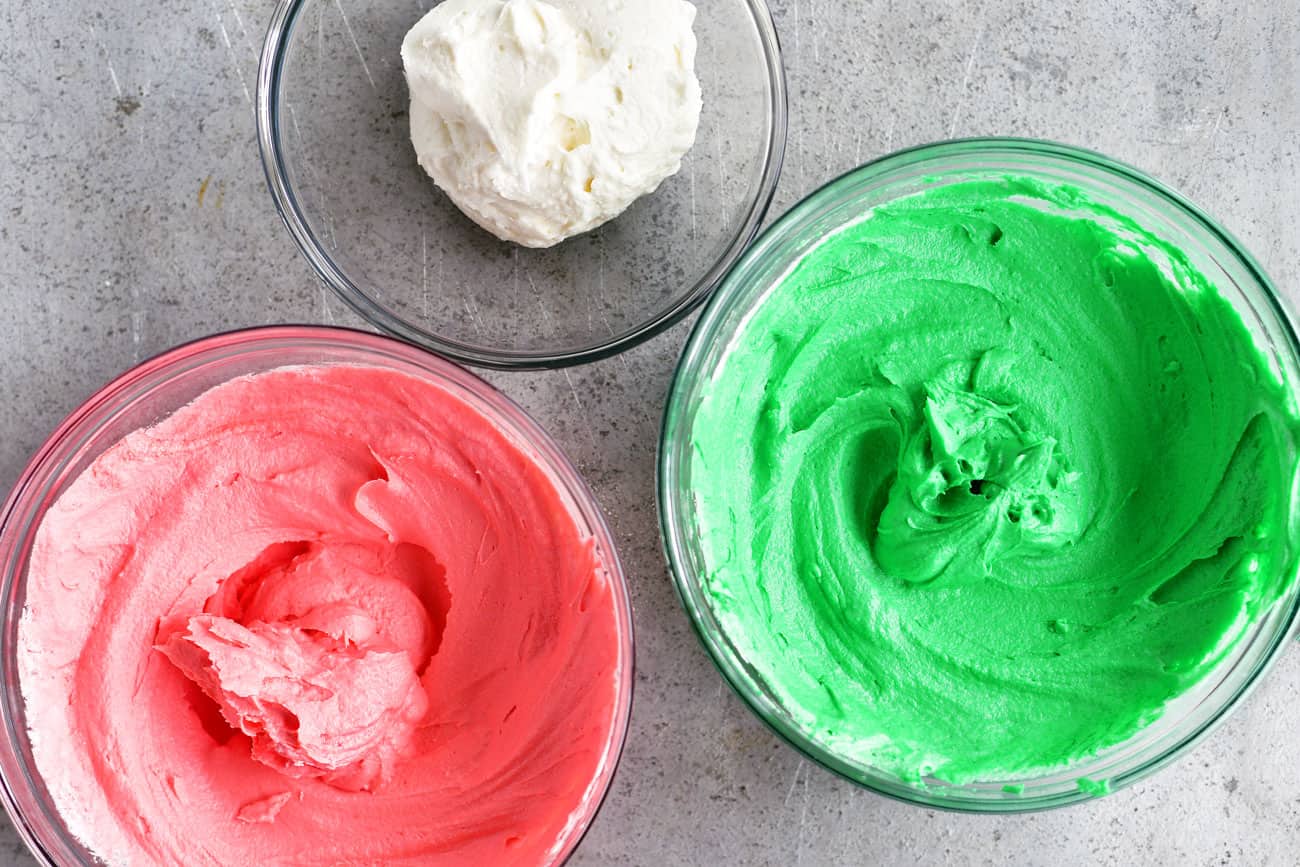 pink, green, and white buttercream frosting in bowls