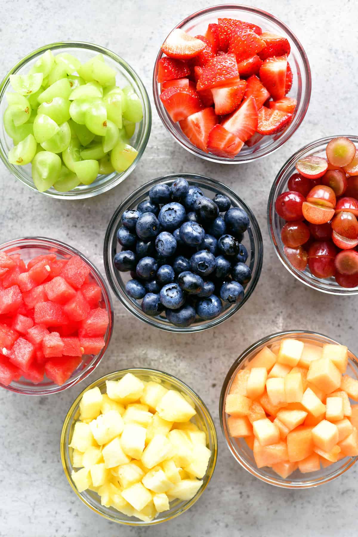 Sliced grapes, diced melon, pineapple tidbits, strawberries, and blueberries in bowls.