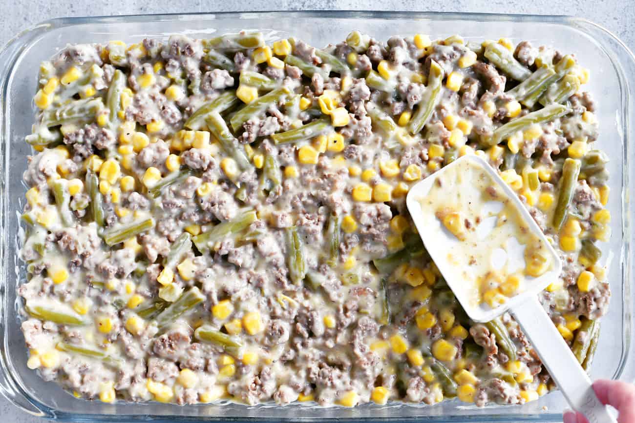 browned meat, green beans and corn spread in a casserole dish