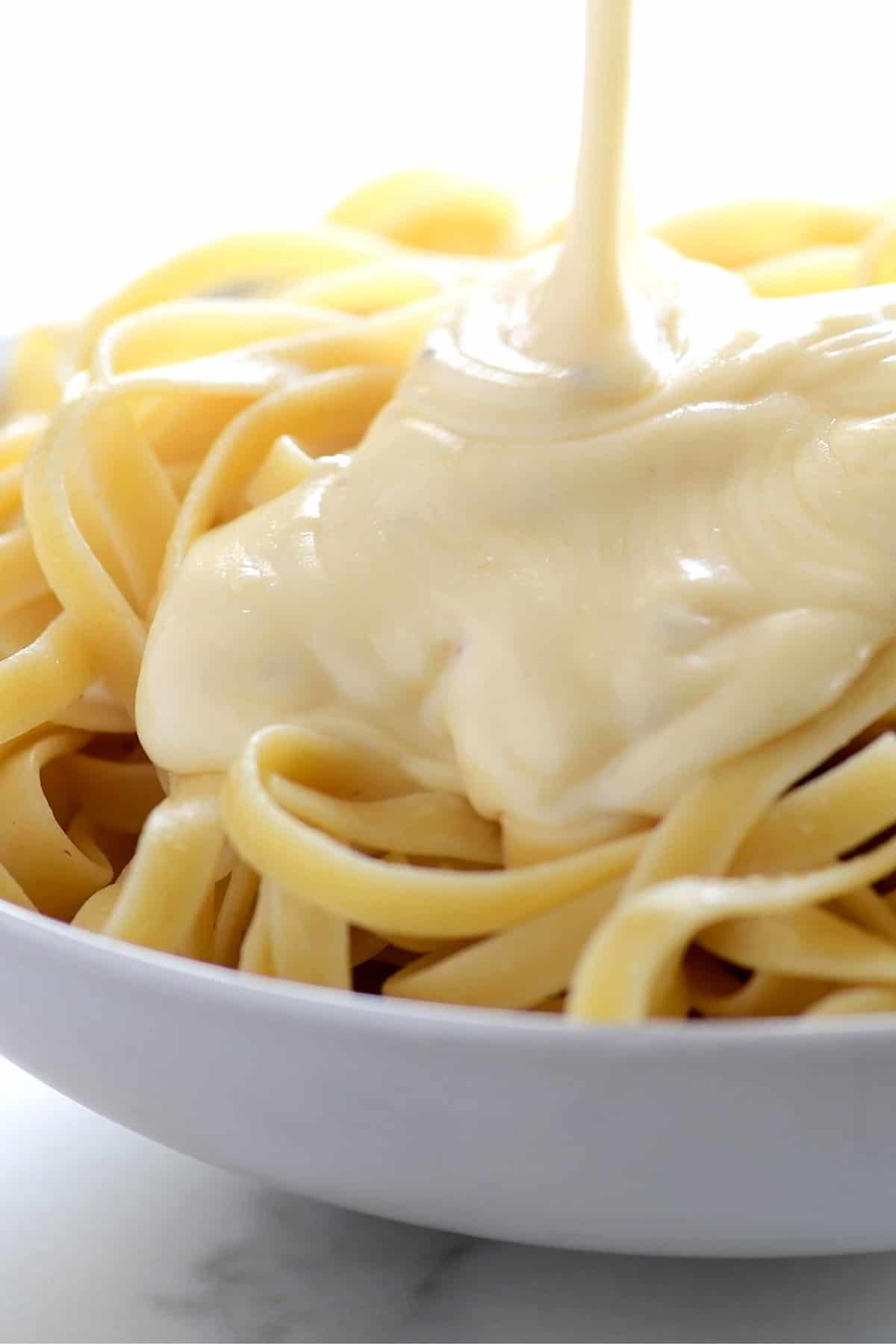 alfredo sauce being poured on fettuccini 