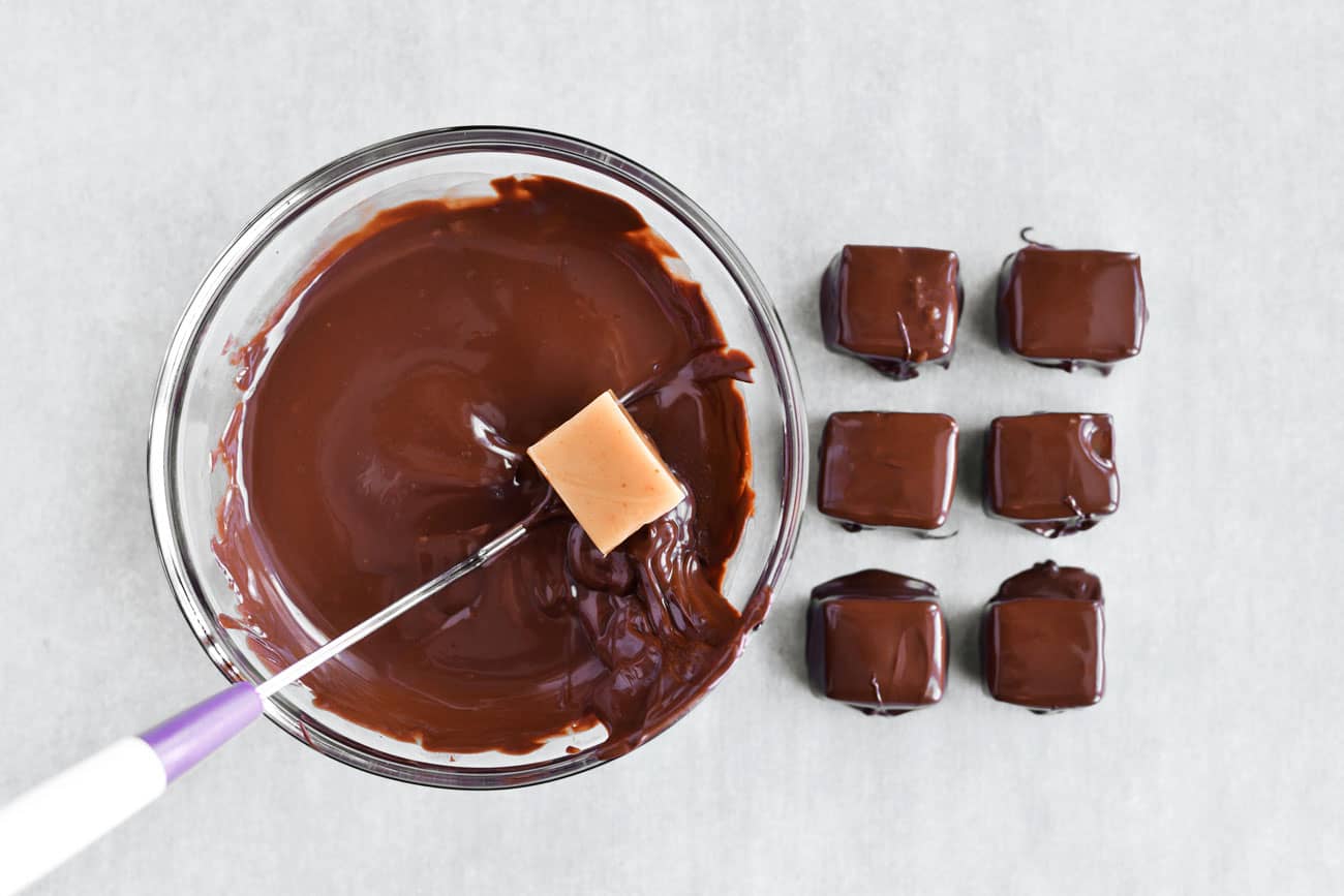 caramel being dipped in melted chocolate
