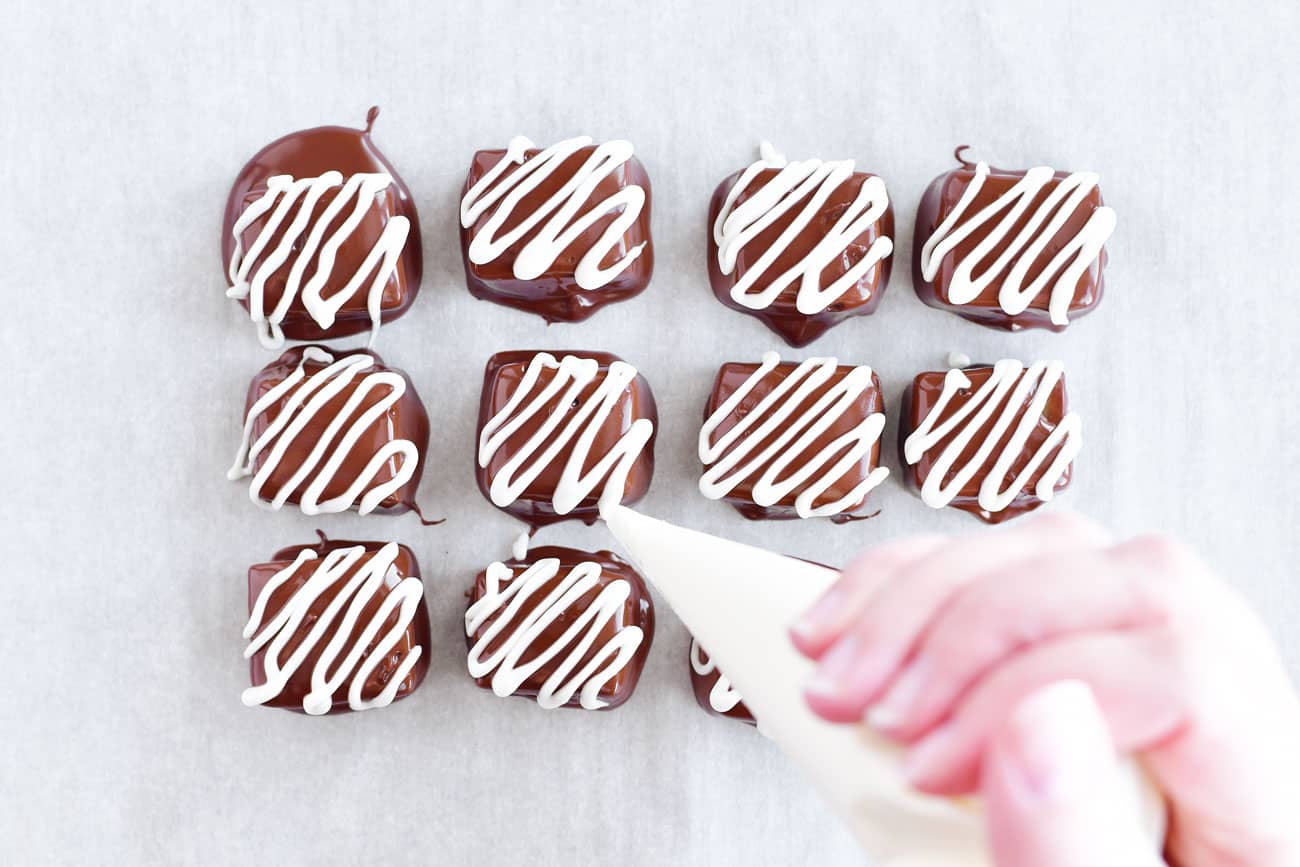 piping white chocolate on caramels