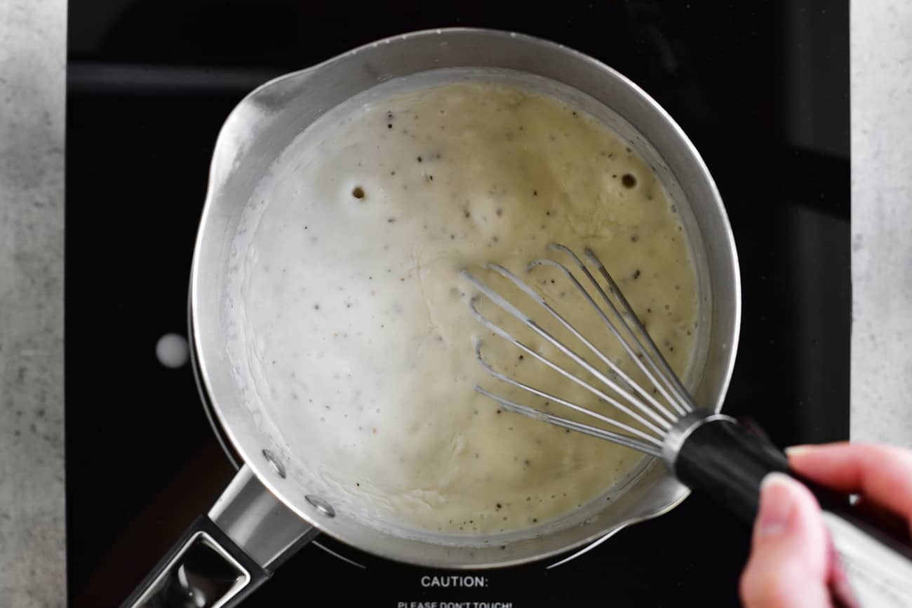 whisking boiling white gravy in saucepan