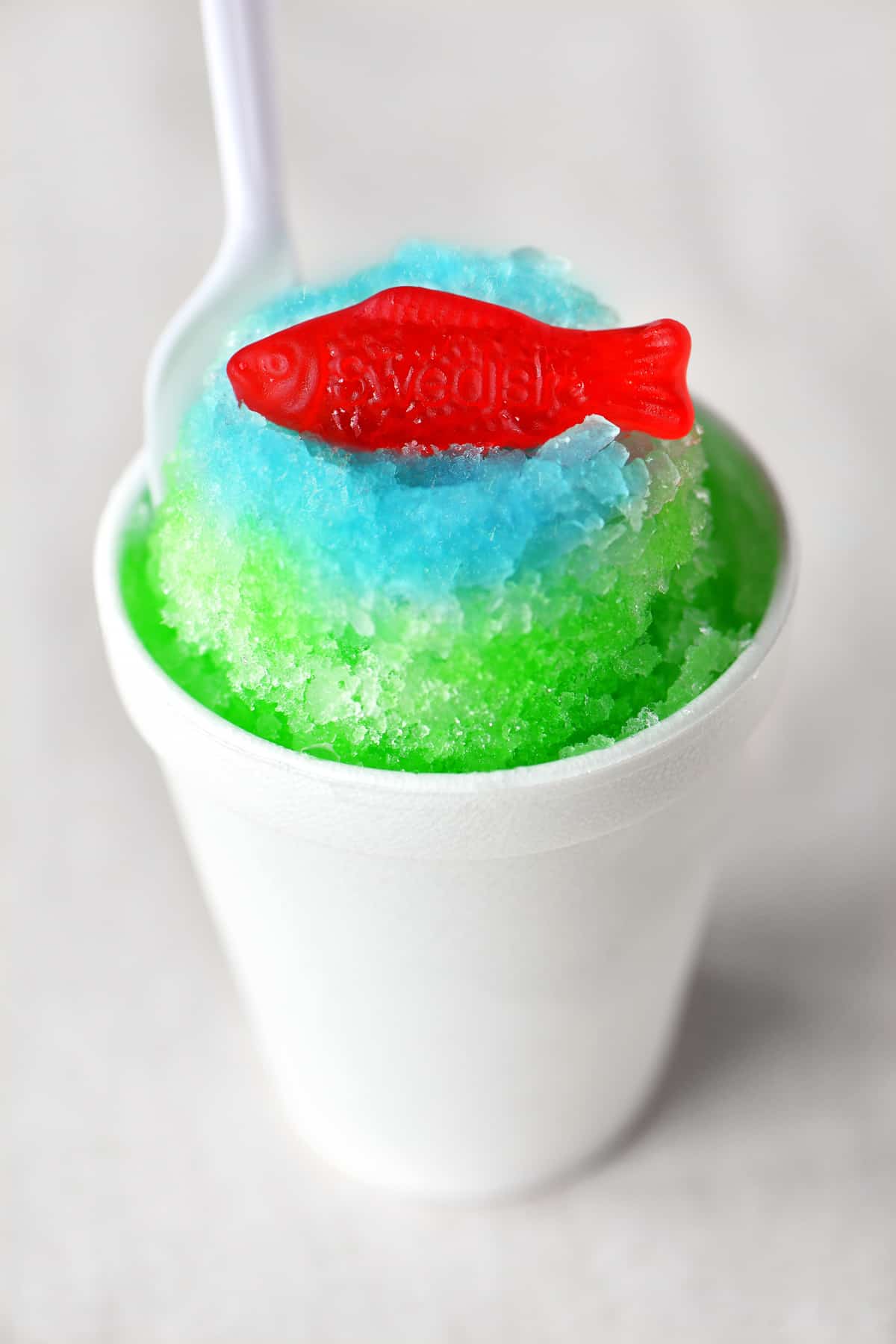 a green and blue shave ice treat with a swedish fish candy on top