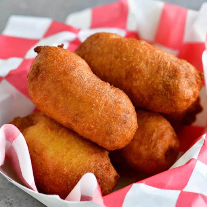 golden crispy mini corn dogs stacked in a red and white paper serving tray