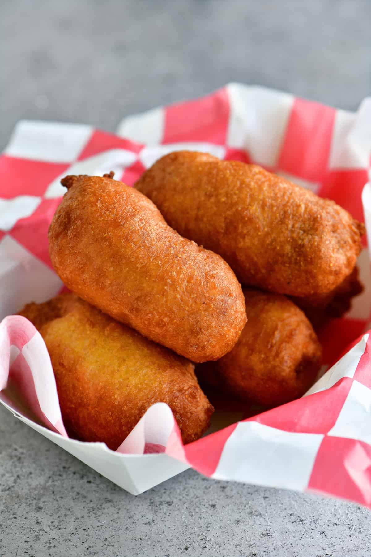 golden crispy mini corn dogs stacked in a red and white paper serving tray