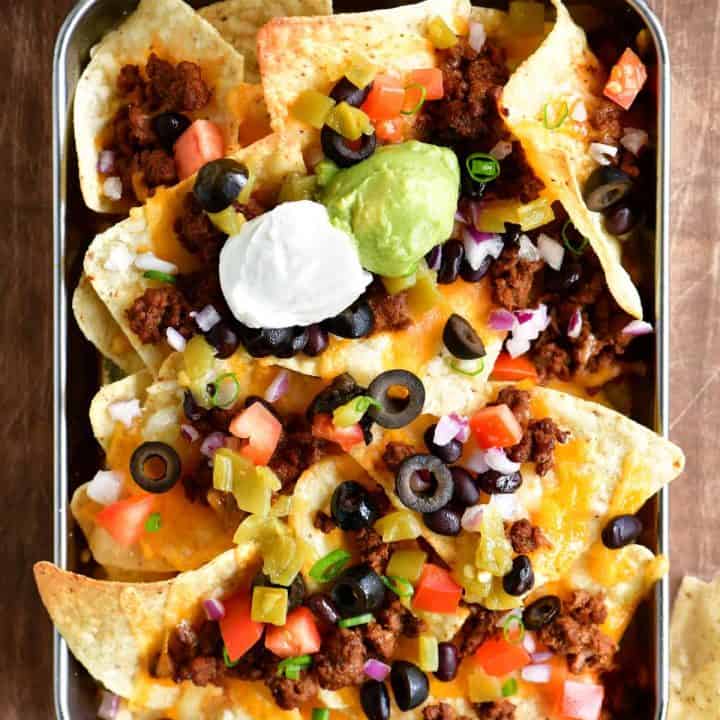a top-down view of the tray of nachos with sour cream, salsa and guacamole dip in bowls