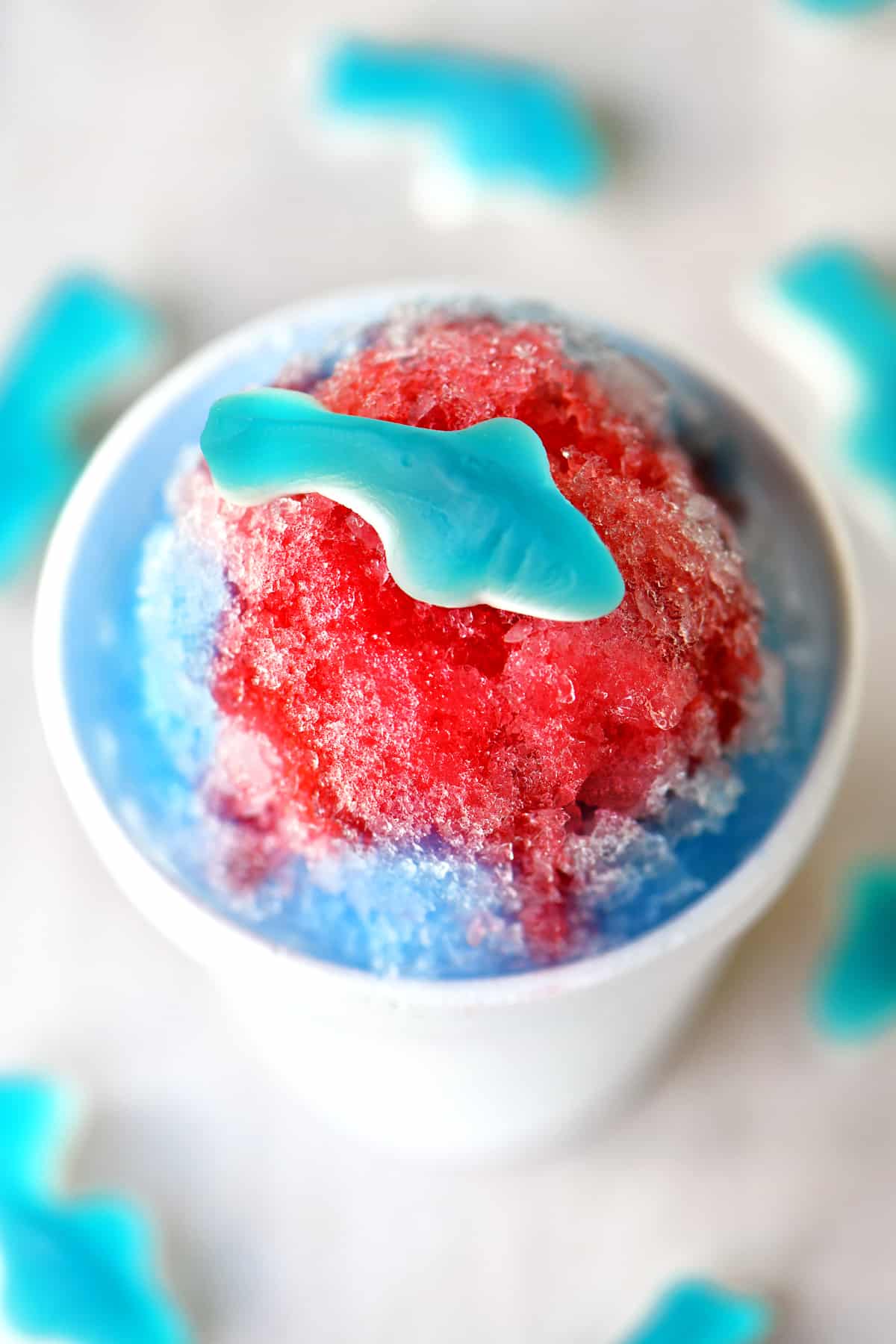 a gummy shark candy on top of a red and blue themed shave ice treat