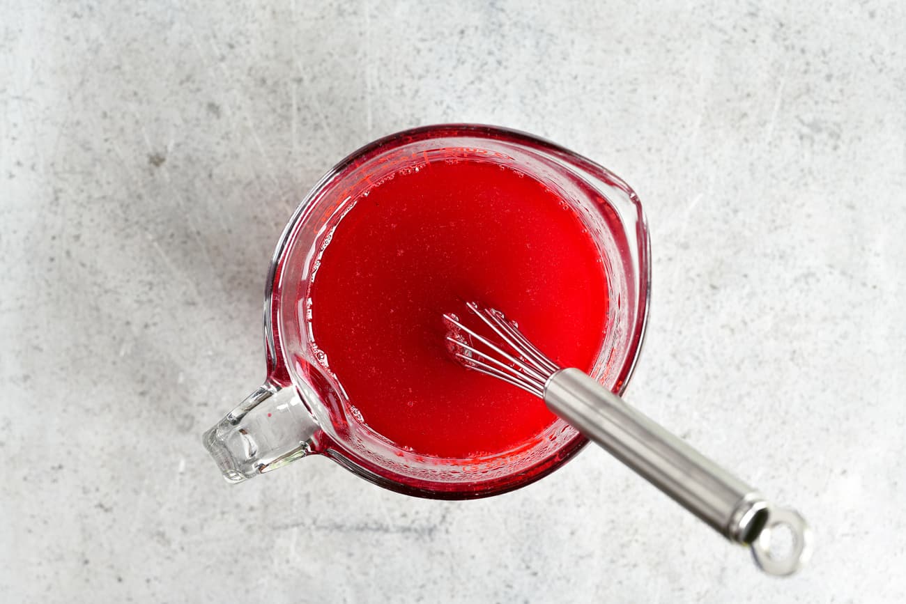 a whisk in a mixing cup with red snow cone syrup