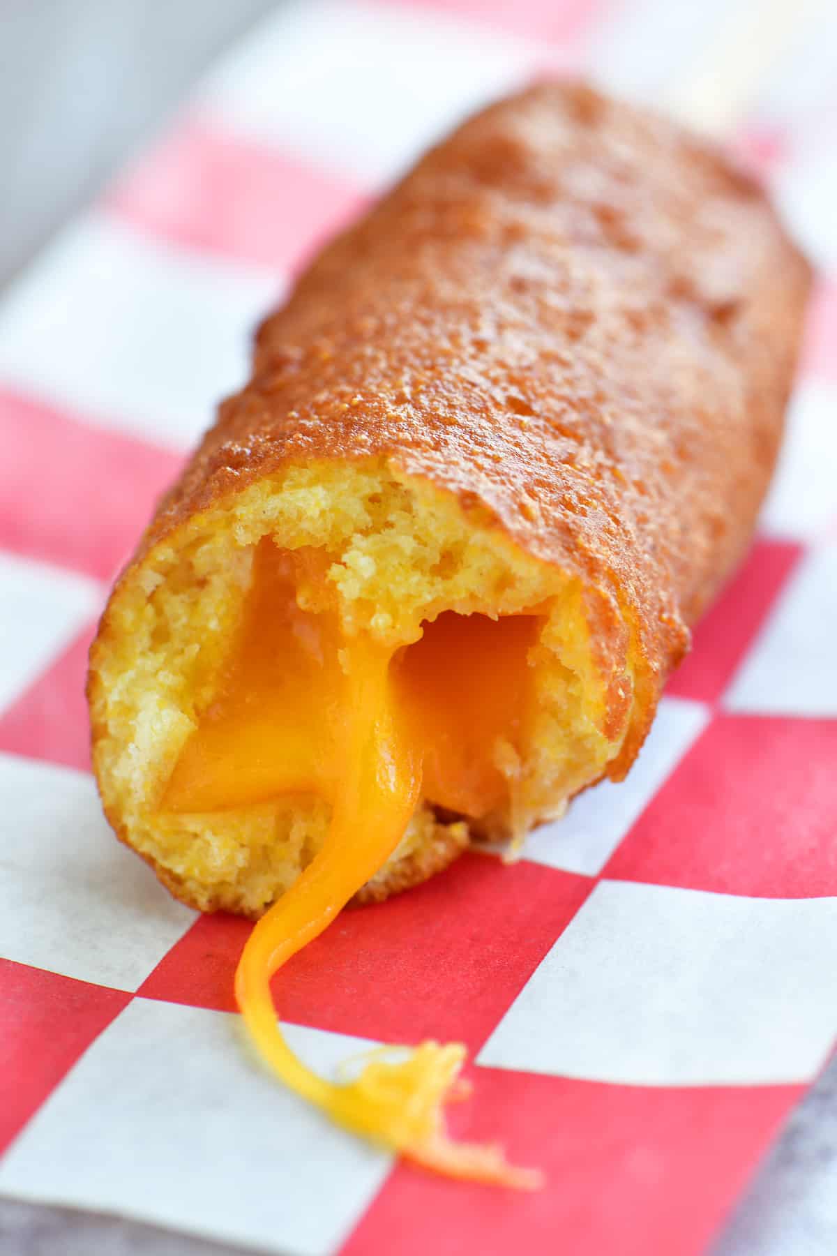 close up photo of fried cheese on a stick with a bite out of it and cheese oozing out