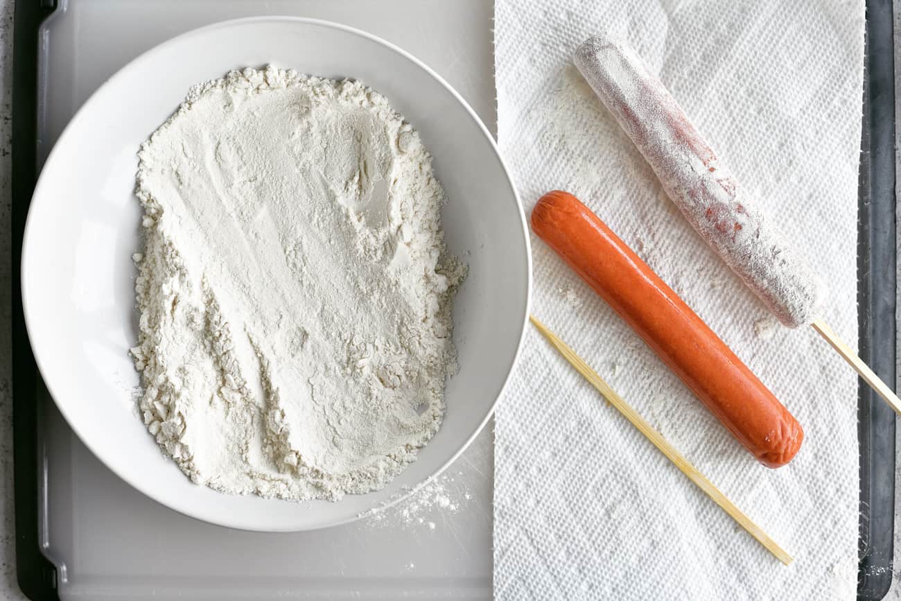 coating a hot dog on a stick in flour