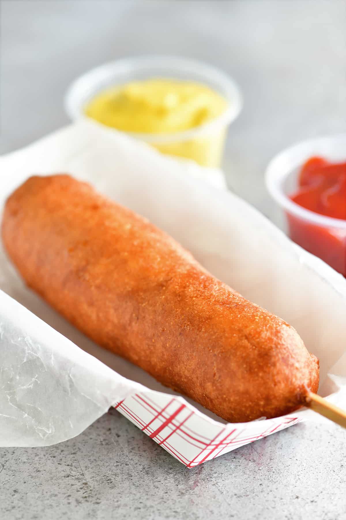 a golden fried corn dog on a red and white paper serving tray