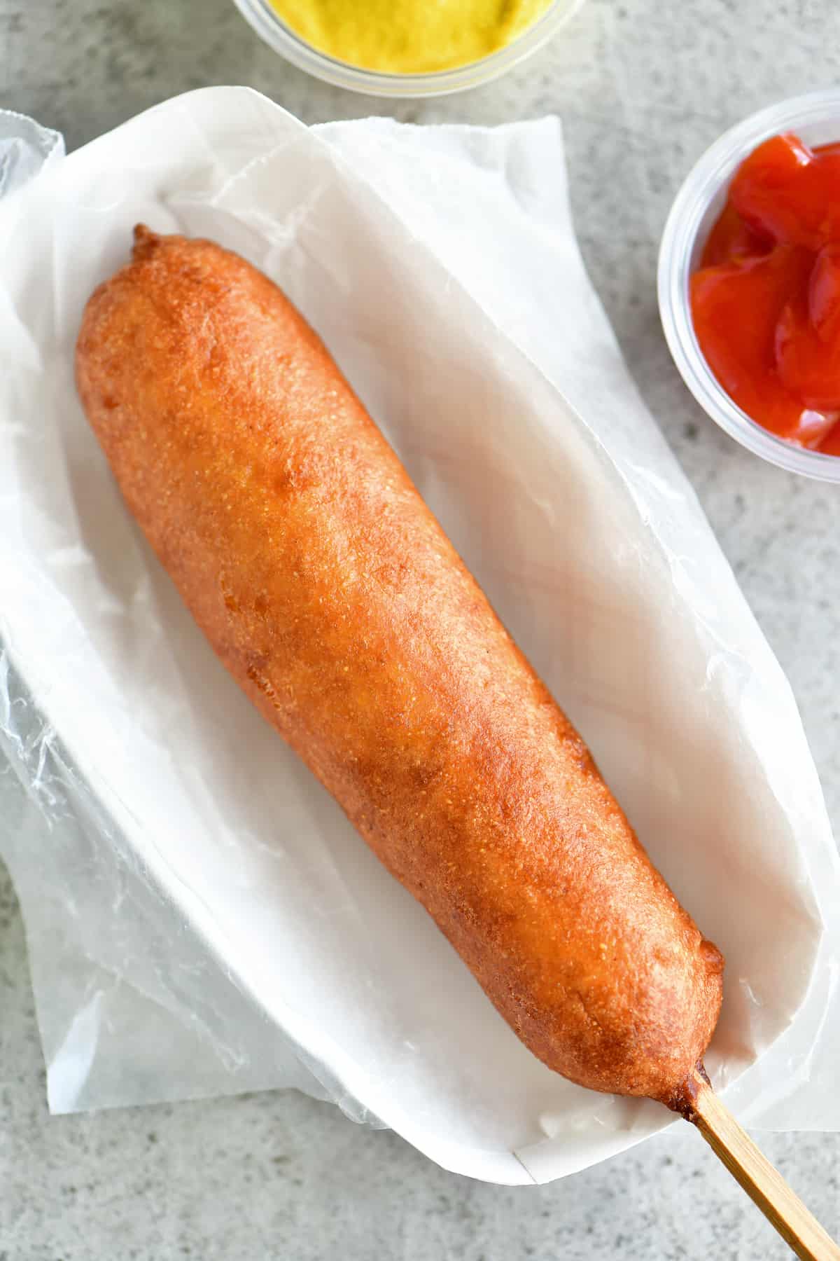 a corn dog on wax paper in a paper serving tray