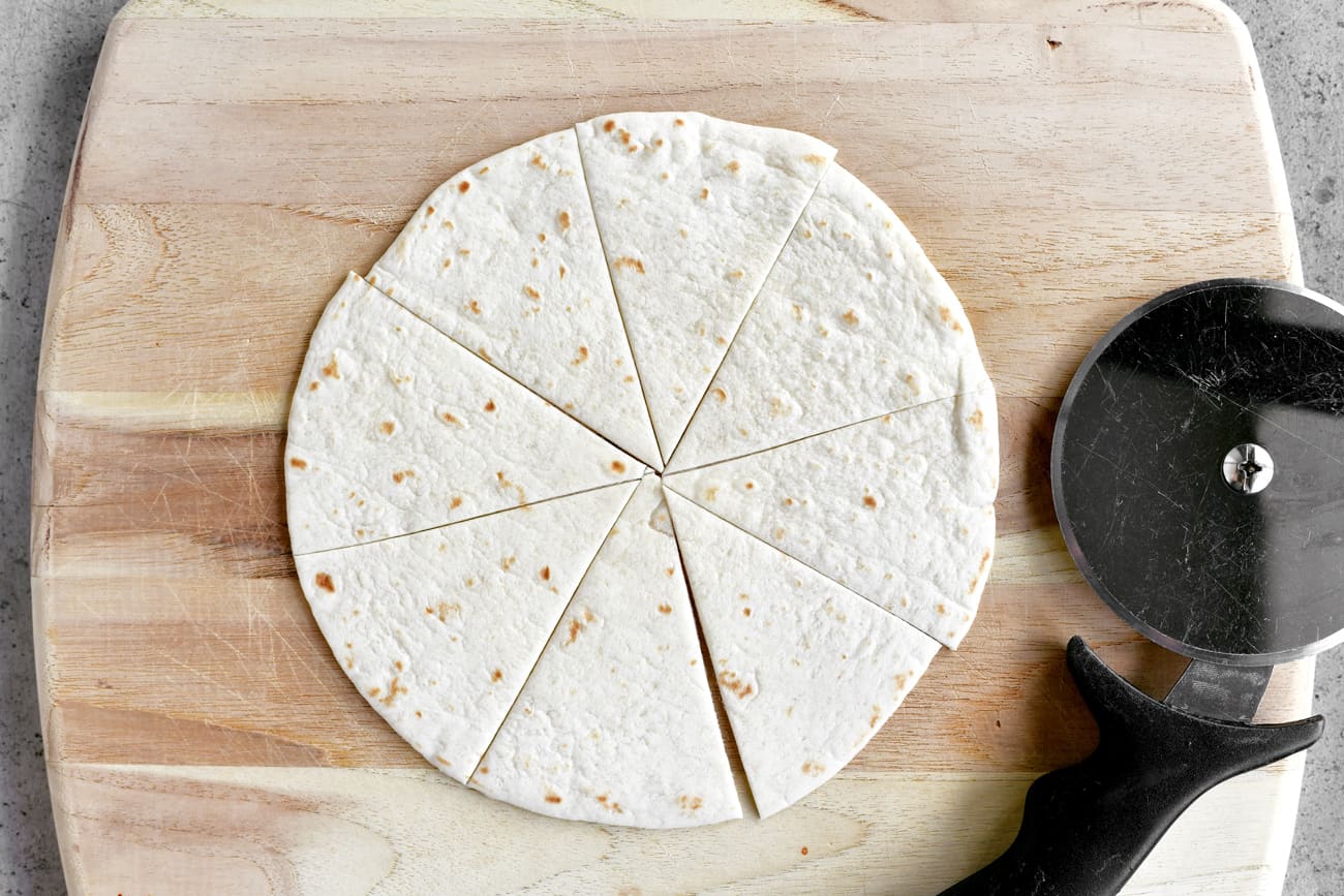 cut flour tortilla with pizza cutter on wood cutting board