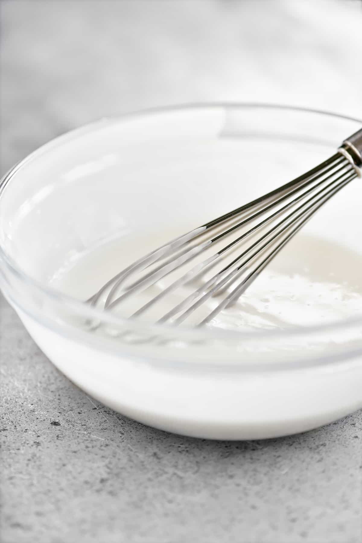 a whisk in a bowl of white glaze