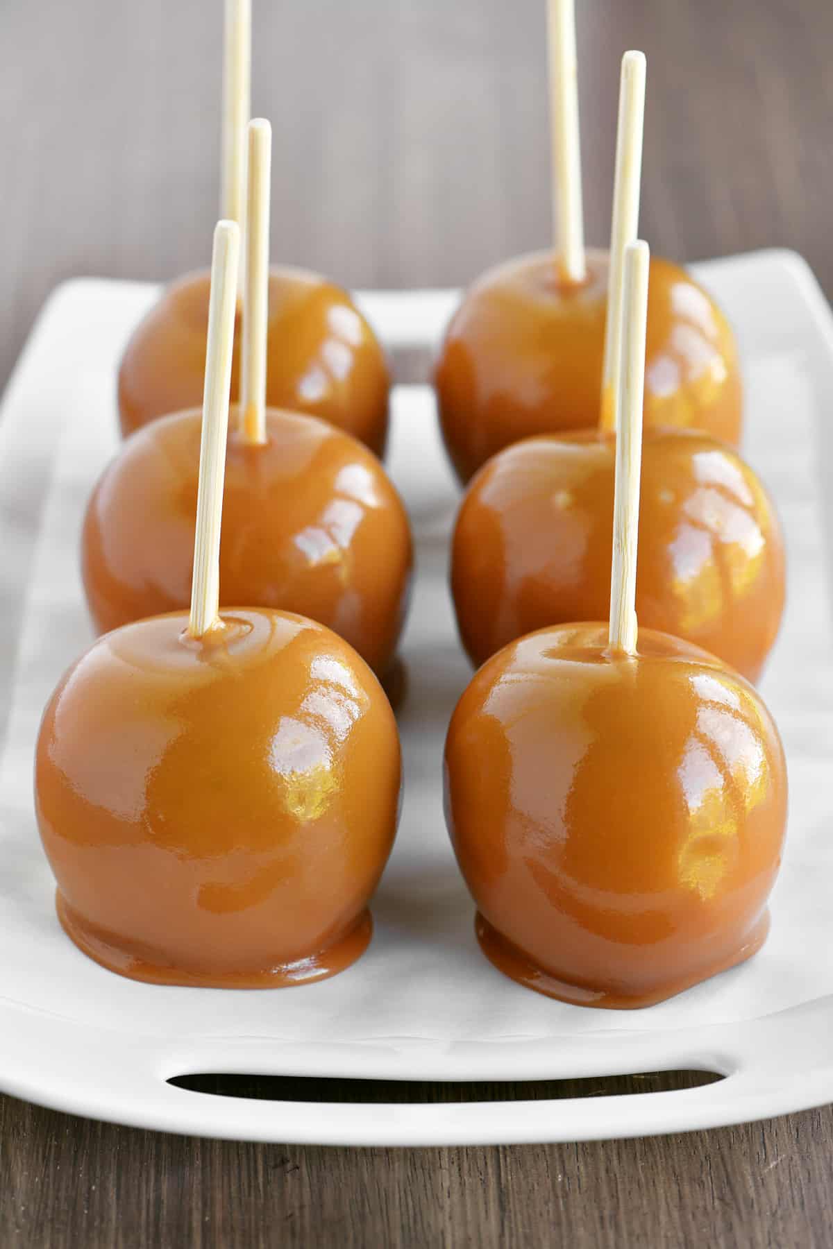 caramel apples lined up on a white serving tray