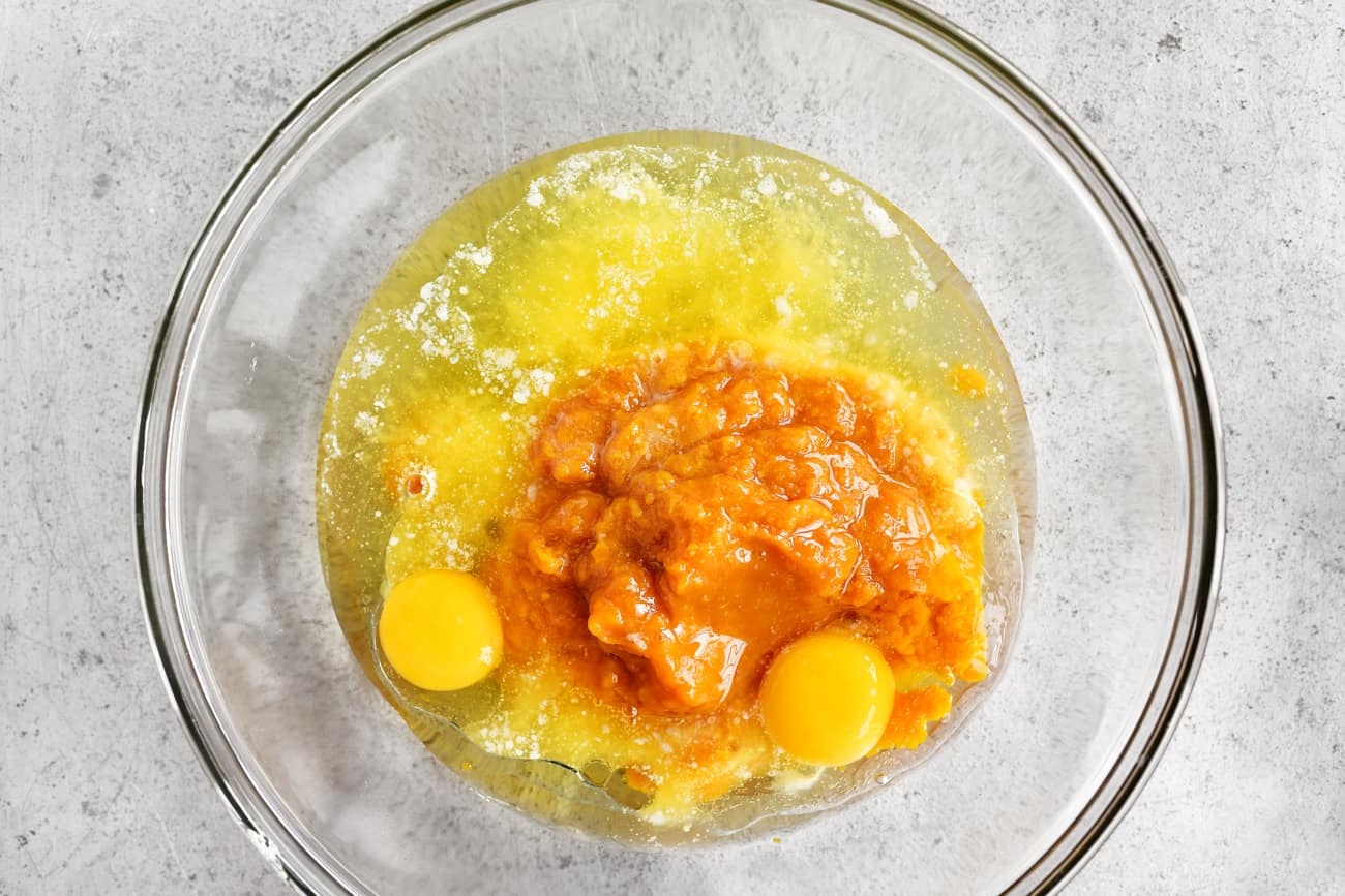 adding eggs and pumpkin puree to a mixing bowl