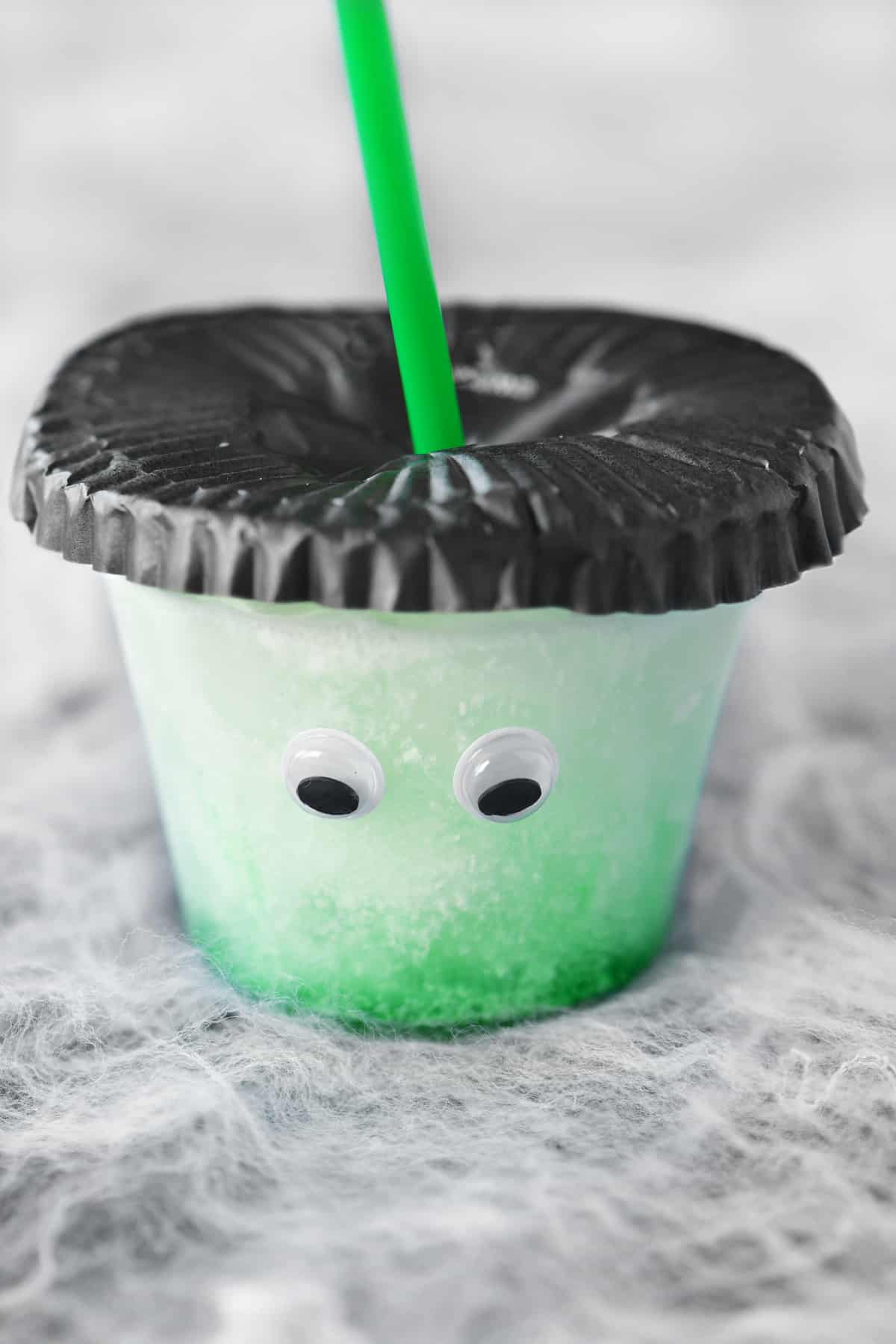 a photo of a green monster Halloween drink for kids with googly eyes and hair