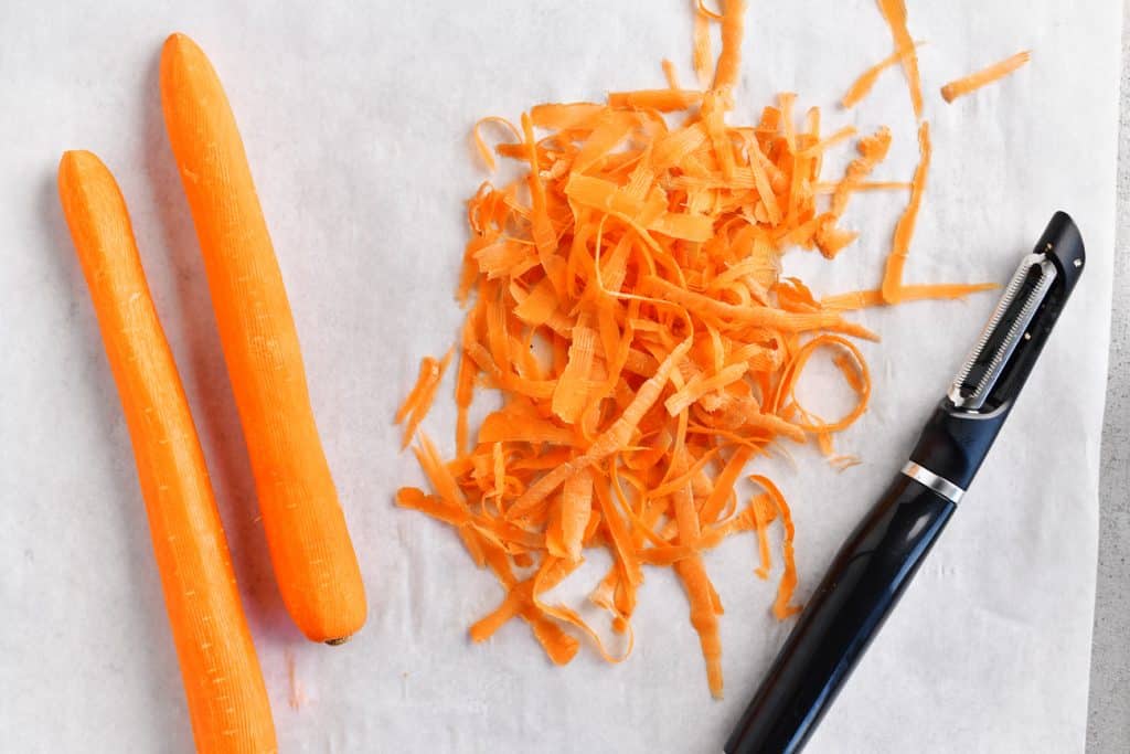 a photo of carrots being peeled over a piece of parchment paper