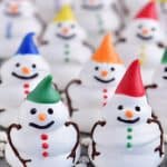 a photo of several meringue snowman cookies with colorful hats and buttons