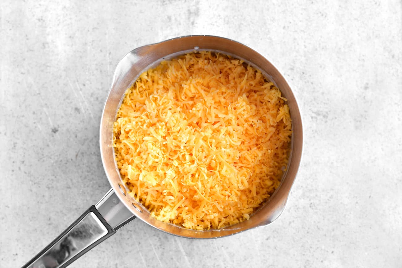 adding shredded cheddar cheese to the saucepan