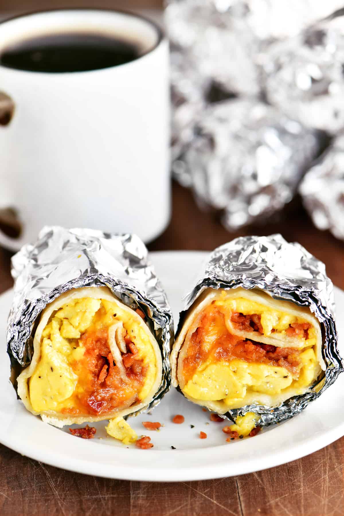 bacon egg and cheese breakfast burrito on a white plate and a mug of coffee